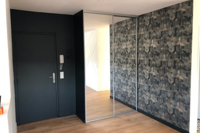 Cette image montre une entrée design avec parquet clair, une porte simple, une porte noire et du papier peint.