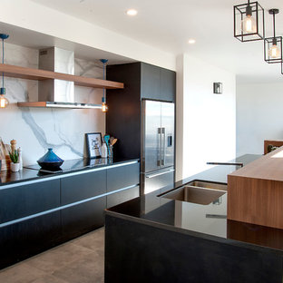 Imagen de cocina comedor de galera, actual, de tamaño medio, con fregadero bajoencimera, encimera de granito, electrodomésticos de acero inoxidable, suelo de baldosas de porcelana, una isla, armarios con paneles lisos, puertas de armario negras, salpicadero de losas de piedra, salpicadero blanco y encimeras negras