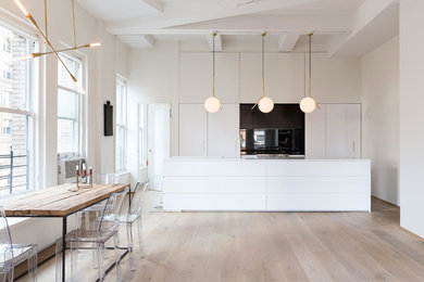 Minimalist kitchen photo in New York with an integrated sink, flat-panel cabinets, white cabinets, stainless steel appliances, an island, black backsplash and stone slab backsplash