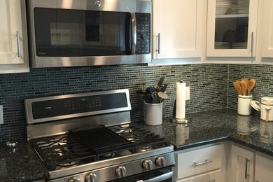 Example of a trendy dark wood floor kitchen design in Other with white cabinets, glass tile backsplash, stainless steel appliances, an island, recessed-panel cabinets and black countertops