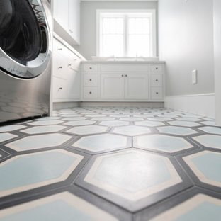 Idées déco pour une grand buanderie éclectique en L dédiée avec un évier de ferme, un placard à porte shaker, des portes de placard blanches, un plan de travail en quartz modifié, une crédence blanche, une crédence en brique, un mur blanc, béton au sol, des machines superposées, un sol bleu, un plan de travail blanc et un mur en parement de brique.