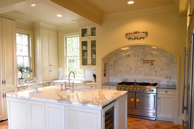 Large elegant u-shaped brown floor and cement tile floor enclosed kitchen photo in Atlanta with white cabinets, granite countertops, multicolored backsplash, stainless steel appliances, an island, a farmhouse sink, recessed-panel cabinets and marble backsplash