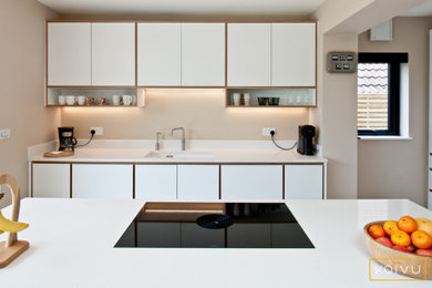 Photo of a large contemporary l-shaped open plan kitchen in Kent with flat-panel cabinets, white cabinets, quartz worktops, integrated appliances, light hardwood flooring and an island.