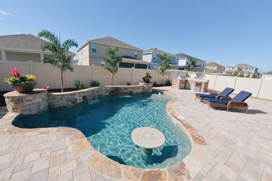 This is an example of a mid-sized tropical backyard custom-shaped pool in Orlando with brick pavers.