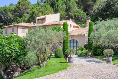 Idée de décoration pour une façade de maison beige méditerranéenne à un étage avec un toit à quatre pans et un toit en tuile.