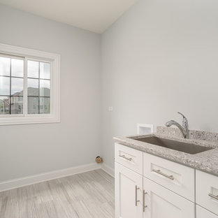 シカゴの中サイズのトランジショナルスタイルのおしゃれな洗濯室 (アンダーカウンターシンク、落し込みパネル扉のキャビネット、白いキャビネット、テラゾーカウンター、グレーの壁、淡色無垢フローリング、左右配置の洗濯機・乾燥機、グレーの床、グレーのキッチンカウンター) の写真