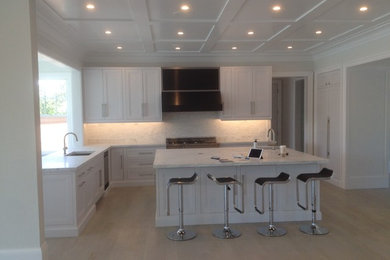 Inspiration for a mid-sized modern u-shaped light wood floor eat-in kitchen remodel in Boston with an undermount sink, recessed-panel cabinets, white cabinets, marble countertops, white backsplash, stone tile backsplash, stainless steel appliances and an island