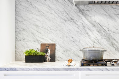 Inspiration for a mid-sized modern single-wall open plan kitchen in Toronto with flat-panel cabinets, marble benchtops, white splashback, marble splashback, stainless steel appliances, light hardwood floors, with island and white benchtop.