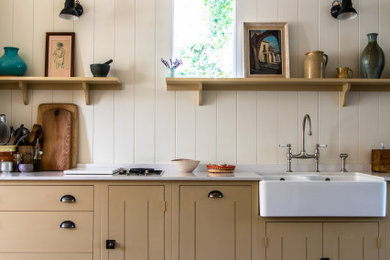 Design ideas for a mid-sized country single-wall open plan kitchen in London with a farmhouse sink, beaded inset cabinets, beige cabinets, marble benchtops, no island, brown floor and white benchtop.