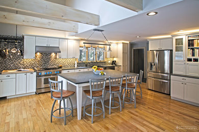 Large mountain style l-shaped light wood floor open concept kitchen photo in Burlington with an undermount sink, shaker cabinets, white cabinets, soapstone countertops, multicolored backsplash, glass tile backsplash, stainless steel appliances and an island