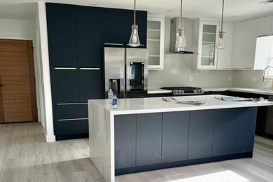 Inspiration for a huge modern l-shaped vinyl floor and gray floor eat-in kitchen remodel in Los Angeles with a drop-in sink, beaded inset cabinets, black cabinets, marble countertops, gray backsplash, black appliances, an island and white countertops