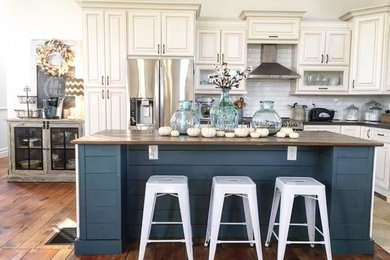 Example of a mid-sized farmhouse medium tone wood floor and brown floor open concept kitchen design in Toronto with an undermount sink, raised-panel cabinets, blue cabinets, quartz countertops, white backsplash, subway tile backsplash, stainless steel appliances and an island
