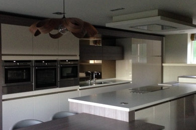 This is an example of a large contemporary kitchen in Manchester with white cabinets, quartzite benchtops, glass sheet splashback, stainless steel appliances and with island.
