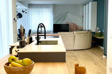 Immagine di un'ampia cucina minimal con lavello sottopiano, ante verdi, top in superficie solida, elettrodomestici neri, parquet chiaro e top bianco