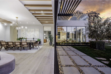 This is an example of a large contemporary open plan dining in Los Angeles with white walls, light hardwood floors, a standard fireplace and a stone fireplace surround.