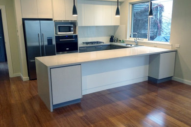 Photo of a mid-sized modern u-shaped eat-in kitchen in Adelaide with a double-bowl sink, flat-panel cabinets, white cabinets, quartz benchtops, white splashback, glass sheet splashback, stainless steel appliances, medium hardwood floors and no island.