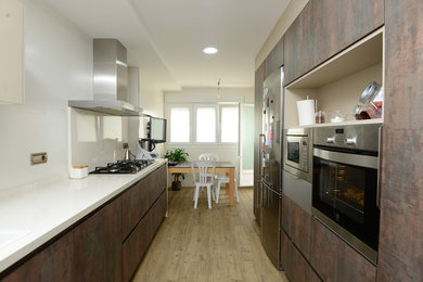 Photo of a large modern galley eat-in kitchen in Other with a double-bowl sink, flat-panel cabinets, quartz benchtops, white splashback, porcelain splashback, stainless steel appliances, medium hardwood floors, brown floor and white benchtop.