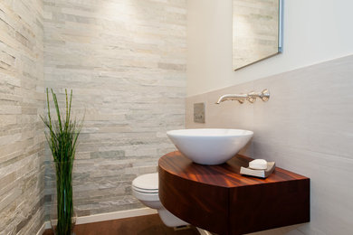Small transitional stone tile and gray tile powder room photo in Seattle with dark wood cabinets, a wall-mount toilet, white walls and a vessel sink