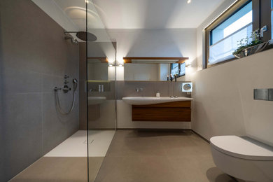 Design ideas for a mid-sized contemporary master bathroom in Other with flat-panel cabinets, dark wood cabinets, a curbless shower, a two-piece toilet, gray tile, ceramic tile, white walls, cement tiles, an integrated sink, grey floor, an open shower, white benchtops, a laundry, a single vanity and a floating vanity.