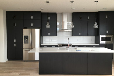 Design ideas for a mid-sized modern galley eat-in kitchen in Calgary with an undermount sink, flat-panel cabinets, black cabinets, white splashback, subway tile splashback, stainless steel appliances, light hardwood floors, with island and quartz benchtops.