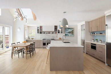 Example of a huge beach style l-shaped light wood floor, beige floor and vaulted ceiling open concept kitchen design in New York with an undermount sink, flat-panel cabinets, light wood cabinets, marble countertops, beige backsplash, marble backsplash, stainless steel appliances, an island and beige countertops