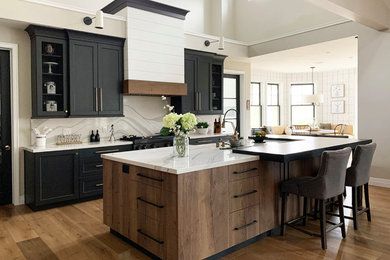 Inspiration for a large farmhouse l-shaped light wood floor and exposed beam open concept kitchen remodel in Santa Barbara with a farmhouse sink, quartz countertops, quartz backsplash, black appliances and an island