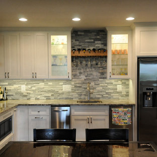 ミネアポリスの大きいシャビーシック調のおしゃれなウェットバー (アンダーカウンターシンク、シェーカースタイル扉のキャビネット、白いキャビネット、御影石カウンター、グレーのキッチンパネル、石タイルのキッチンパネル、ライムストーンの床、茶色い床、マルチカラーのキッチンカウンター) の写真