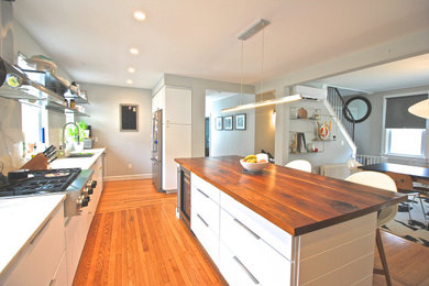 Eat-in kitchen - mid-sized contemporary galley light wood floor eat-in kitchen idea in Providence with an undermount sink, flat-panel cabinets, white cabinets, solid surface countertops, white backsplash, stone slab backsplash, stainless steel appliances, an island and white countertops