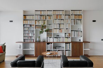 Imagen de biblioteca en casa moderna grande sin chimenea y televisor con paredes blancas y suelo de madera clara