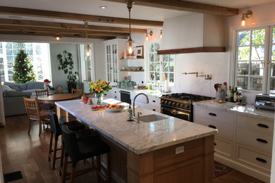 Photo of a large traditional single-wall separate kitchen in San Francisco with a farmhouse sink, beaded inset cabinets, medium wood cabinets, marble benchtops, white splashback, subway tile splashback, black appliances, light hardwood floors, with island and white benchtop.