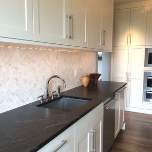 На фото: огромная параллельная кухня в современном стиле с кладовкой, врезной раковиной, фасадами с утопленной филенкой, белыми фасадами, столешницей из талькохлорита, белым фартуком, фартуком из каменной плитки, техникой из нержавеющей стали и темным паркетным полом без острова с
