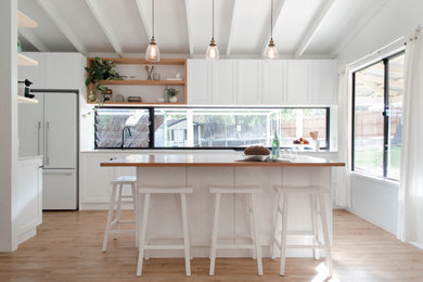 Inspiration for a mid-sized contemporary galley open plan kitchen in Perth with an undermount sink, shaker cabinets, white cabinets, quartz benchtops, window splashback, white appliances, medium hardwood floors, with island, brown floor and white benchtop.