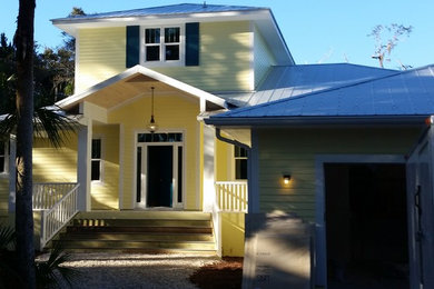 This is an example of a large arts and crafts two-storey yellow house exterior in Tampa with wood siding and a metal roof.