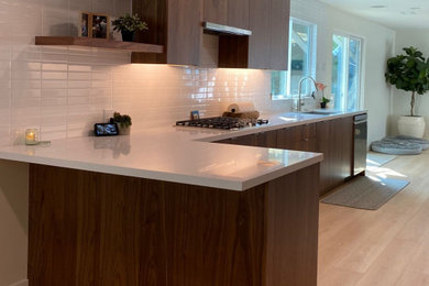 サンディエゴにあるモダンスタイルのおしゃれなキッチン (フラットパネル扉のキャビネット、中間色木目調キャビネット、白いキッチンパネル、サブウェイタイルのキッチンパネル、白いキッチンカウンター) の写真