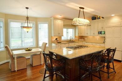Inspiration for a large transitional l-shaped medium tone wood floor eat-in kitchen remodel in Columbus with an undermount sink, raised-panel cabinets, beige cabinets, granite countertops, beige backsplash, paneled appliances and an island