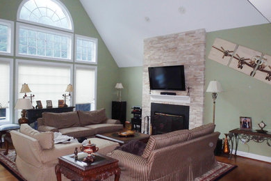 Example of a large minimalist loft-style medium tone wood floor living room design in Philadelphia with green walls, a standard fireplace, a stone fireplace and a wall-mounted tv