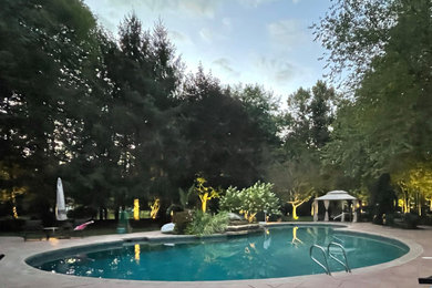 Diseño de piscina campestre grande en patio trasero con paisajismo de piscina y adoquines de hormigón