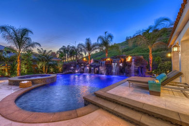 Photo of a large tropical backyard custom-shaped natural pool in Orange County with a water feature and concrete pavers.