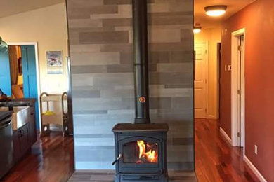 Example of a transitional medium tone wood floor family room design in DC Metro with gray walls, a wood stove and a tile fireplace