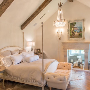 Cette image montre une grande chambre parentale traditionnelle avec un mur blanc, un sol en bois brun, une cheminée double-face, un manteau de cheminée en pierre et un sol marron.