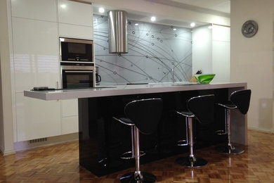 This is an example of a contemporary single-wall eat-in kitchen in Adelaide with flat-panel cabinets, white cabinets, granite benchtops, metallic splashback, glass sheet splashback, stainless steel appliances and with island.