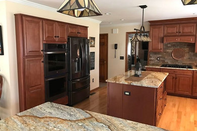 Open concept kitchen - transitional l-shaped light wood floor open concept kitchen idea in Orange County with raised-panel cabinets, medium tone wood cabinets, quartzite countertops, brown backsplash, black appliances, an island and a single-bowl sink