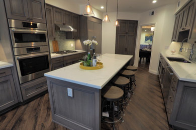 Mid-sized transitional galley dark wood floor and brown floor enclosed kitchen photo in Los Angeles with an undermount sink, recessed-panel cabinets, gray cabinets, marble countertops, gray backsplash, subway tile backsplash, stainless steel appliances, an island and gray countertops