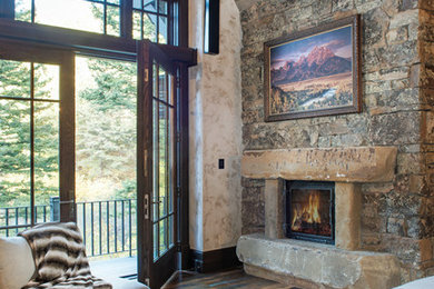 Large mountain style master dark wood floor bedroom photo in Other with beige walls, a standard fireplace and a stone fireplace