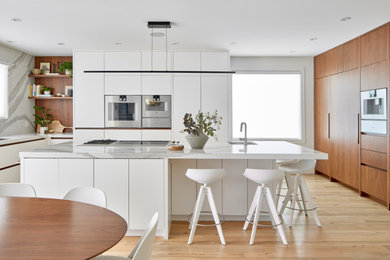 Photo of a large midcentury kitchen in Toronto with an undermount sink, flat-panel cabinets, quartz benchtops, engineered quartz splashback, panelled appliances, light hardwood floors, with island and white benchtop.