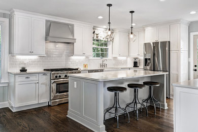 Photo of a contemporary kitchen in Charleston with a farmhouse sink, shaker cabinets, white cabinets, quartz benchtops, white splashback, porcelain splashback, stainless steel appliances, dark hardwood floors and with island.