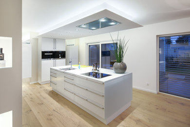 Offene Moderne Küche mit flächenbündigen Schrankfronten, weißen Schränken, braunem Holzboden und Kücheninsel in Sonstige