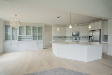 Elegant single-wall light wood floor and brown floor open concept kitchen photo in Portland with a drop-in sink, white cabinets, granite countertops, blue backsplash, subway tile backsplash, stainless steel appliances, an island and white countertops