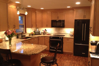 Inspiration for a mid-sized transitional l-shaped medium tone wood floor enclosed kitchen remodel in Philadelphia with an undermount sink, shaker cabinets, light wood cabinets, granite countertops, beige backsplash, ceramic backsplash, black appliances and a peninsula