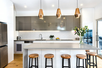 Photo of a contemporary l-shaped kitchen in Melbourne with an undermount sink, flat-panel cabinets, white splashback, stainless steel appliances, medium hardwood floors, brown floor and with island.